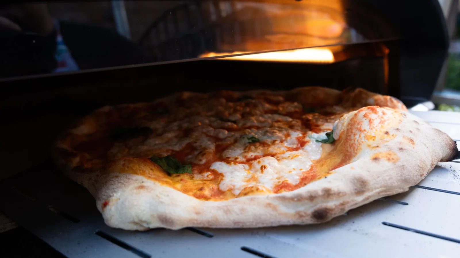 A pizza cooking in the mouth of the oven, flames behind it
