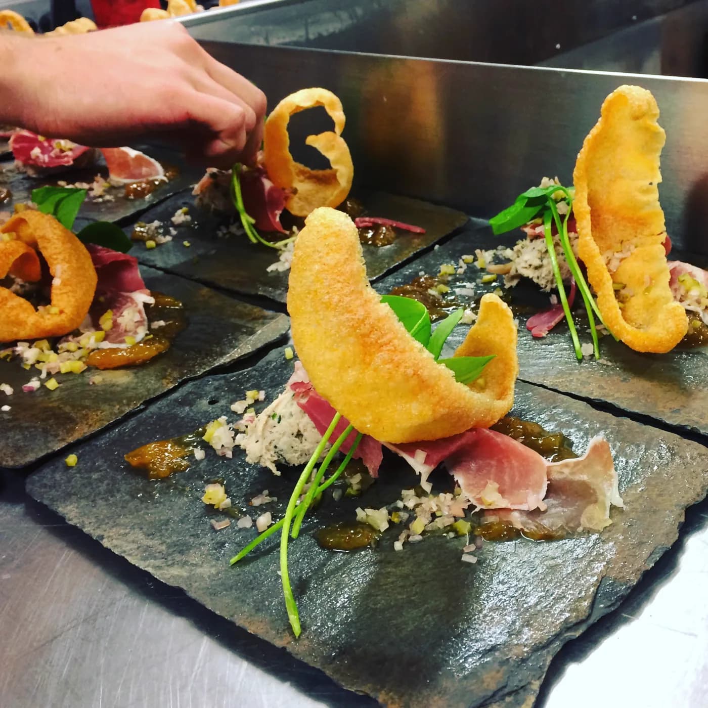 A pork and ham course being finished with herbs and a crisp on slate