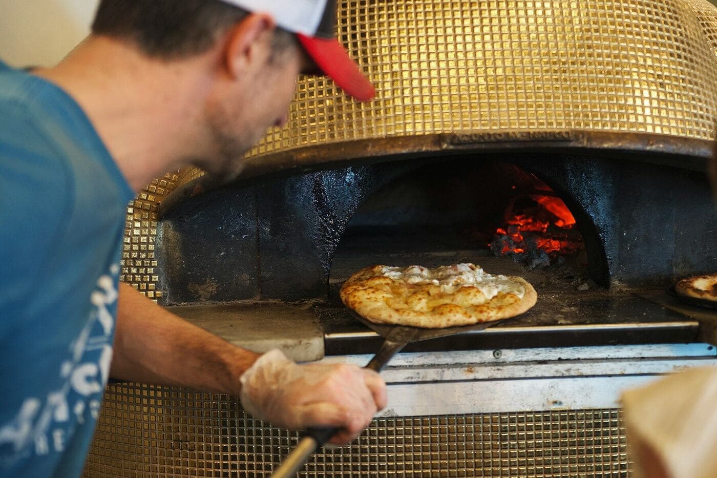 A cook sliding a pizza into the oven on a peel
