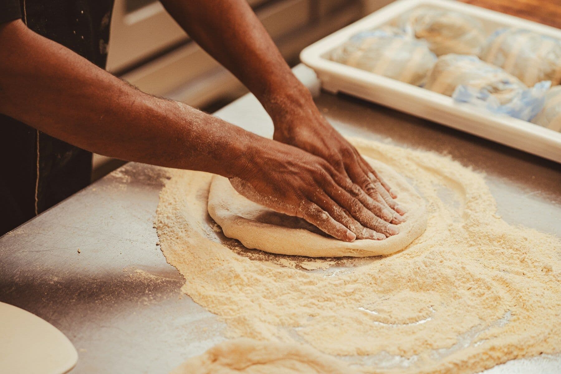 Hands pressing out a sourdough base on a floured surface