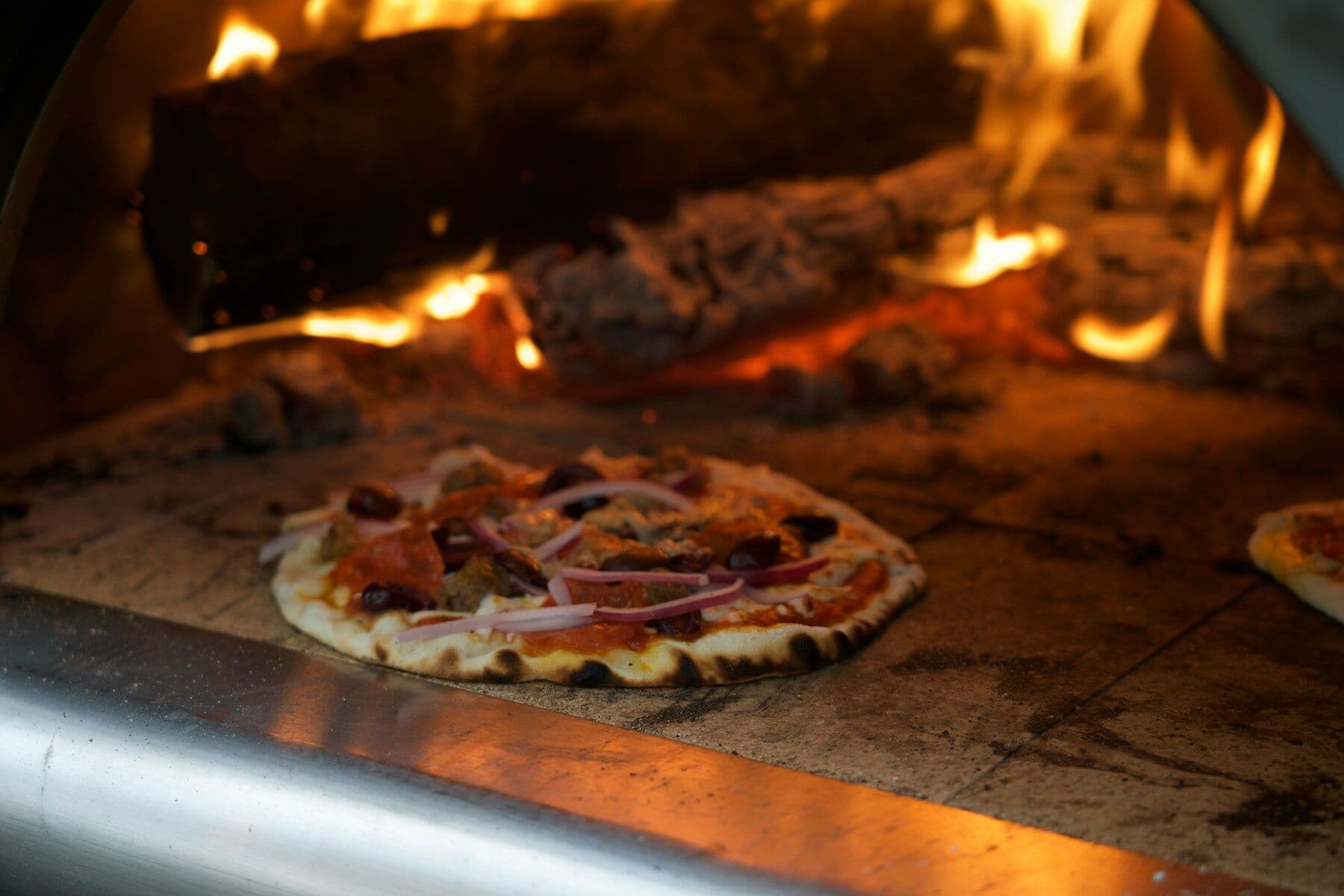 A pizza cooking in the mouth of the oven, flames behind it